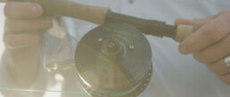 A closeup view of a fishing reel attached to a rod. Although lens flare has blown out the image somewhat, white writing on the reel says 