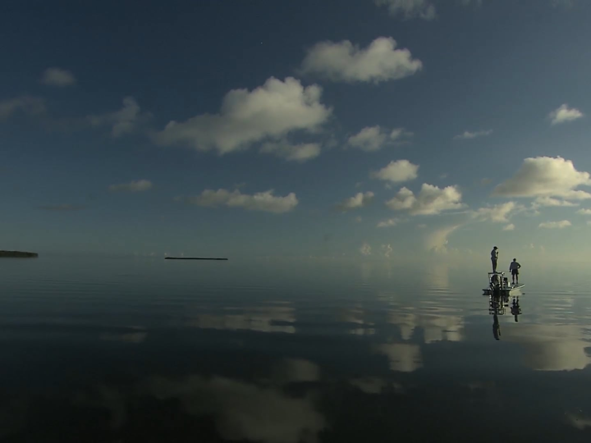 A large expanse of water reflects the sky and clouds. On the right side two people stand on a skiff, one on the deck and one on the poling platform.